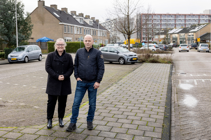 Linda Twigt en Jaap van Wuijckhuijse staan op straat in een woonwijk met brede wegen, veel lege parkeerplekken en weinig bomen of ander groen